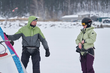 A middle-aged man and woman, snowsurfers, husband and wife, stand, rest and talk. They went snowsurfing on a cloudy winter day.