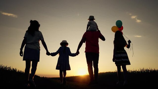 Happy family concept. Fun walk with balloons in nature. Silhouette people summer holiday outdoors. Family walks together holding hands along a rural road in the park. Family picnic in spring in nature