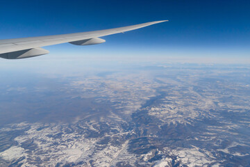 Wing of an airplane jet flying above clouds with blue sky from the window in traveling and transportation concept. Nature landscape background.