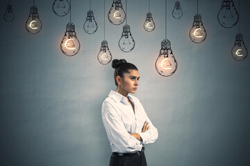 Pensive young european businesswoman standing on concrete wall background with glowing lamp sketches and euro sign. Business ideas, income and success concept. - Powered by Adobe