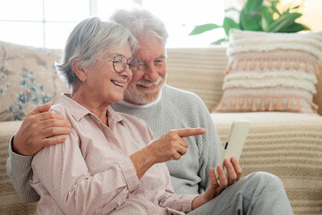 Beautiful caucasian senior couple sitting on the floor at home using mobile phone, modern retired elderly people using technological devices to see funny videos