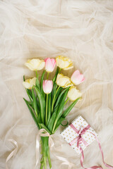 A bouquet of spring tulip flowers and a gift box with a pink bow on a beige fabric background for mother's day Flat lay