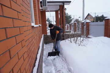 A man cleans snow in the winter in the courtyard of the house.