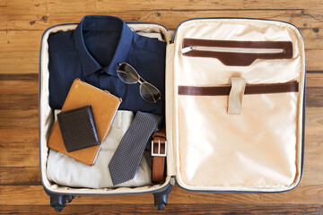 All packed and ready to go. High angle shot of a suitcase packed with various essentials for a...