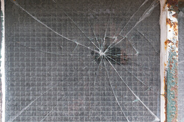 A reinforce glass window has cracks spreading from a central impact point.
