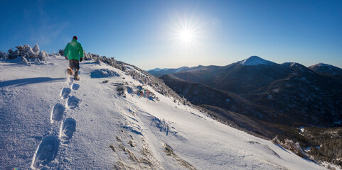 Sun shining over snowshoer traversing snow on summit of Mount Colden, New York, USA
