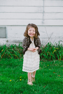Portrait of three year old smiling girl wearing white dress and standing on grass