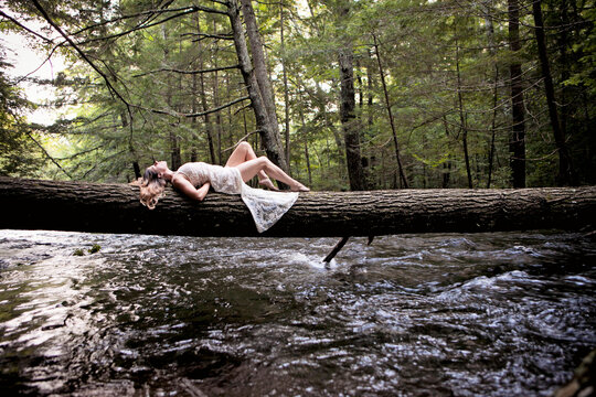 A woman in a white dress lays on a log across a river