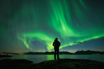 Silhouette of person watching Northern Lights - Aurora Borealis  over coastline, AustvÃ¥gÃ¸y, Lofoten Islands, Norway