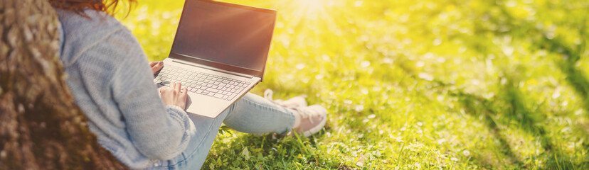 Woman with laptop sitting on the grass in the natural park. - 576605997