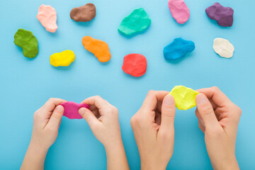 Mother and child hands holding and kneading modeling clay on blue table background. Pastel color....