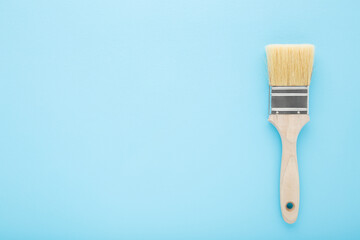 New paint brush on light blue table background. Pastel color. Closeup. Preparation for repair work...