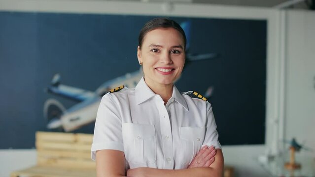 Front view of woman wearing uniform standing in classroom, looking at camera, smiling. Young, pretty female pilot, instructor wearing uniform. Concept of flying airplane.