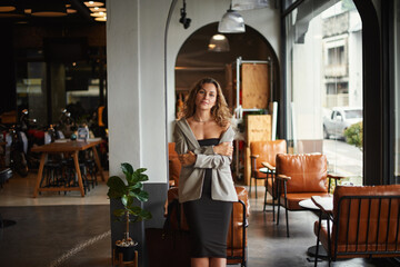 Happy young woman sitting in modern cafe and smiling, looking at the camera - 576611310