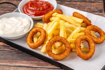 Onion rings and french fries with ketchup and mayonnaise on wooden table