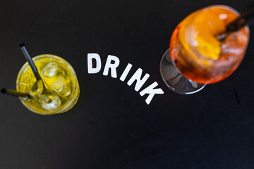 Due cocktail di un bar elegante fotografati dall'alto su uno sfondo nero e con la scritta "drink" al centro