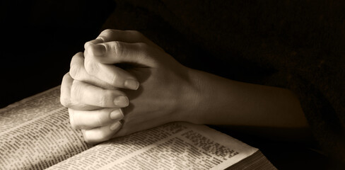 Hands clasped in prayer near an open book