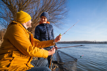 Father and son are fishing on sunny winter day. Freshwater fishing. Teenage boy is learning to fish.