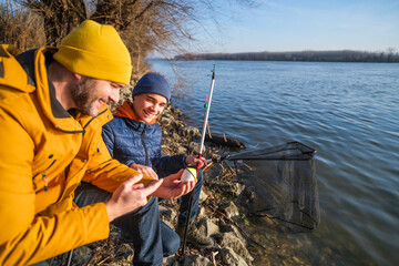 Father and son are fishing on sunny winter day. Freshwater fishing. Teenage boy is learning to fish.