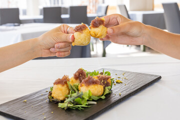Due clienti di un ristorante elegante mentre brindano con due bocconcini di baccalà fritti guarniti con cipolla caramellata 