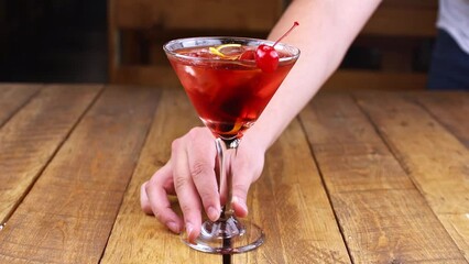 Waiter rotating a red fruit cocktail on a wooden table,