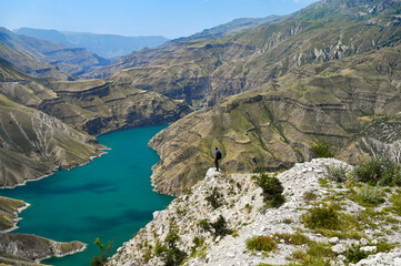 A tourist stands on a mountain and looks at the blue-green river in the Sulak Canyon on a sunny summer day. Dagestan