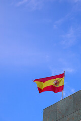Spanish Flag Waving on Top of A Building with Blue Sky as the Background

