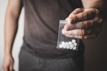 Man's hand holds transparent plastic packet with white pills lsd, drug dealer selling drugs. Drug abuse and addiction concept - obrazy, fototapety, plakaty