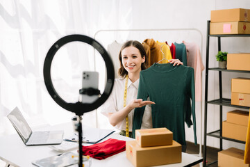 Fototapeta na wymiar Fashion blogger concept, Young Asian women selling clothes on video streaming.Startup small business SME, using smartphone or tablet taking receive and checking..
