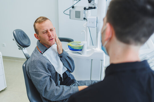 A Young Dentist Doctor Tells A Male Patient About Dental Care. A Man Was Sitting In A Dental Chair At A Doctor's Appointment. Modern Dental Treatment