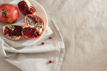 Pomegranates on beige tablecloth, background with copy space. Fresh red fruits on plate.