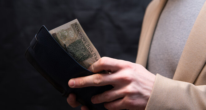 a man dressed in a smart casual style holds Polish money in his hand. Polish economy and finance