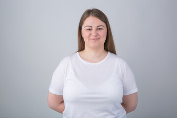 Obraz premium Cheerful plus size model posing in studio. Young Caucasian overweight woman wearing white t-shirt looking in camera with a smile