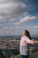 Vertical image of a young woman in fleece lining opening her arms and taking a breath of fresh air...
