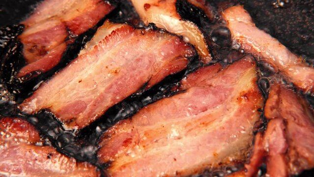 Frying Bacon Slices in a Pan. Crispy Pieces of Delicious Red Thin Smokey Bacon Fried in a Hot Skillet. Traditional Breakfast. Smoked Bacon Rasher or Strip Being Cooked. Grill. Fat High Calorie Food.