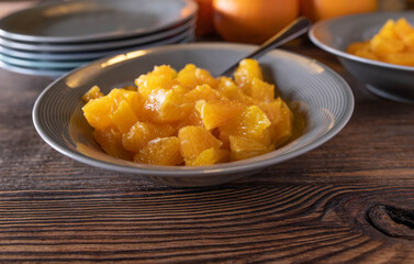 Chopped oranges in a bowl with spoon for dessert or snack on wooden table. Closeup, front view with copy space