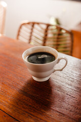 Black strong coffee in a white cup. Hot Americano on a wooden background in sunlight