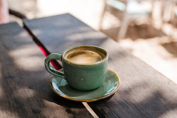 Strong hot coffee in a green cup on a wooden table. Hot Americano on the background of sunlight