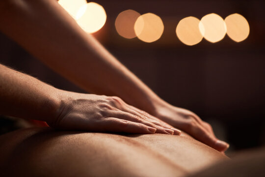 Closeup image of masseuse applying light strokes when applying oil on back of client
