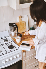 Asian woman in white clothes preparing morning beverage, pouring hot coffee from cezve to white cup - 576633769