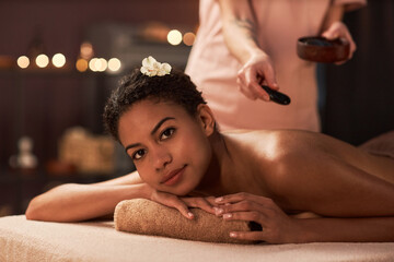 Obraz na płótnie Canvas Young woman geeting stress relief hot stones massage in spa salon