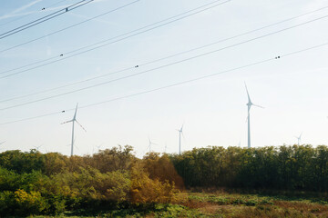 13 wind turbines producing electricity above forest with multiple high voltage electricity lines above them - green forest location