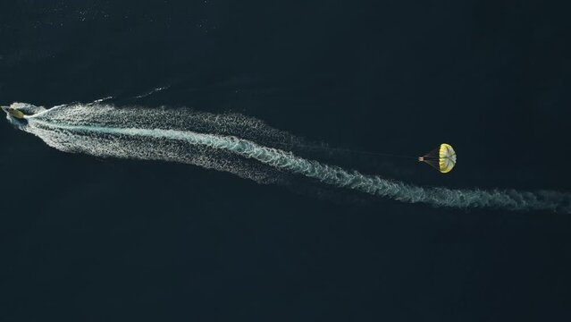 Aerial view of a person doing parasail with a motorboat along the coast in Sicily, Italy.