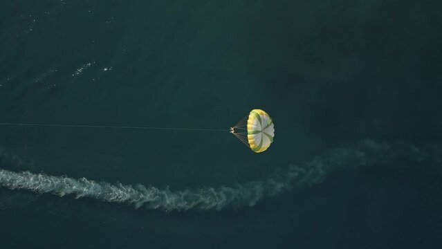 Aerial view of a person doing parasail with a motorboat along the coast in Sicily, Italy.