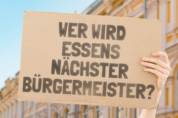 The phrase " Who's the next mayor of Essen? " on a banner in men's hands blurred the background. Election. City management. Politics. Urban. Voter. Candidate