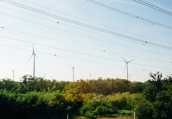 Multiple fleet park of wind turbines producing electricity above forest with multiple high voltage...