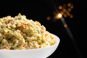 Olivier russian salad - a classic recipe with mayonnaise, an incredible taste, on a black background, with bokeh of sparklers for christmas and new year - obrazy, fototapety, plakaty