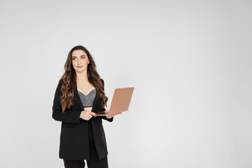 young businesswoman in a black jacket holds a laptop in her hands while standing on a gray background