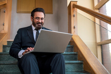 Senior corporate man using laptop at office stair