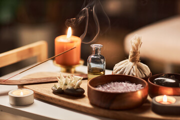 Obraz na płótnie Canvas Burning incense stick on tray next to bottle of massage oil, salt scrub and herbal bag
